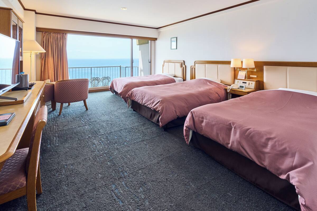 Une chambre d’hôtel avec deux lits, un bureau, une chaise et une vue sur l’océan.