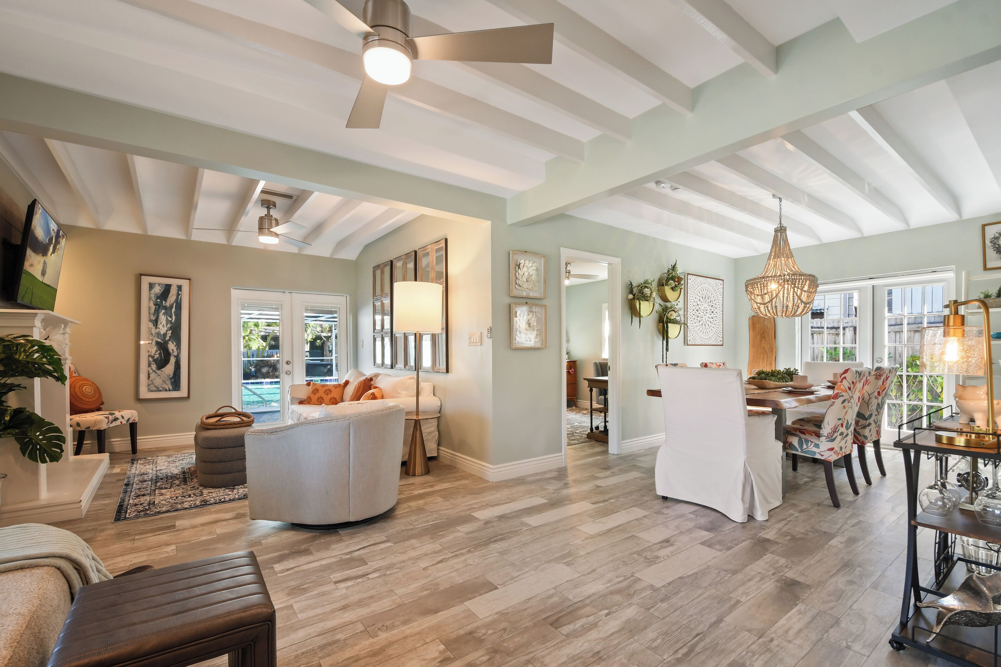 A spacious living room with a high ceiling, a dining area with a chandelier, and a view of the outdoors through large windows.