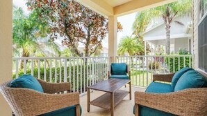 A covered outdoor seating area with wicker furniture and a table, surrounded by a white railing, overlooking a garden with palm trees. - Spacious 4-bedroom villa in nice Kissimmee Florida (Kissimmee)