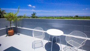 Een terras met een witte tafel en twee metalen stoelen, een plant in pot en uitzicht op het landschap.