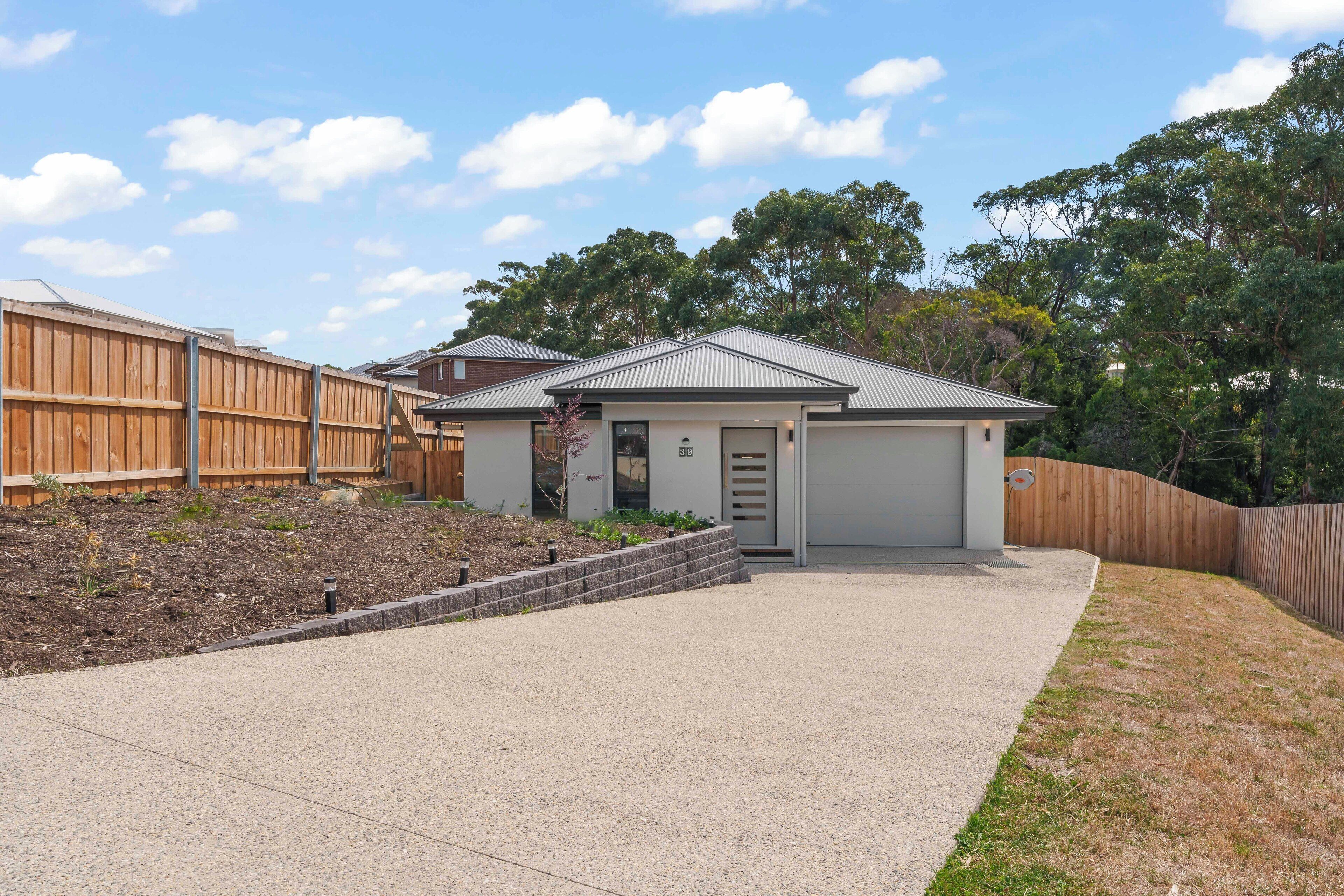 A residential property with a paved driveway, a small garage, and a wooden fence.