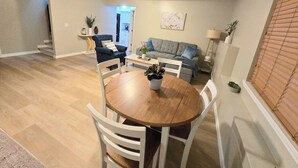 A dining area with a round wooden table and white chairs, a grey sofa, and a lamp in the background. - 2 bed 2bath guest house with private entrance, near light rail & Seattle (Lynnwood)