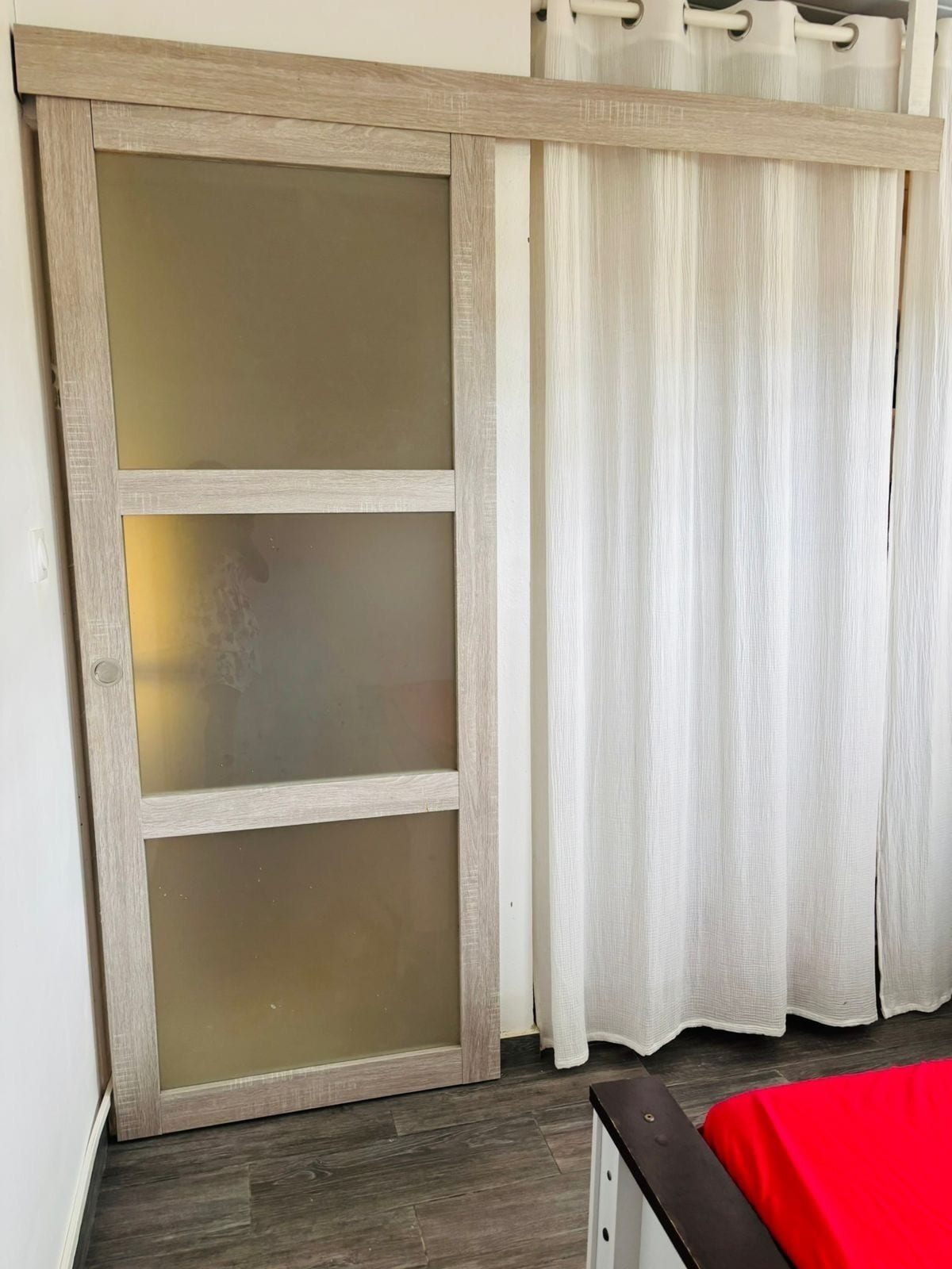 Una stanza con una porta scorrevole, un letto con copripiumino rosso e una tenda.