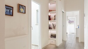 A hallway with a white door, a shelf with books and decorative items, and a small window. - Homiday- House L -Wood beams and comfort by the sea (Livorno)