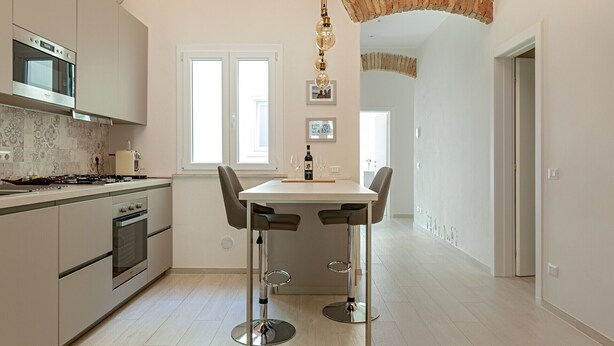 A modern kitchen with a central island, stainless steel appliances, and a hanging light fixture. - Homiday- House L -Wood beams and comfort by the sea (Livorno)