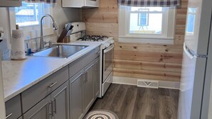 A compact kitchen with wooden panel walls, a microwave, a gas stove, and a refrigerator.