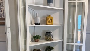 A white cabinet with multiple shelves and a glass door, containing various decorative items.