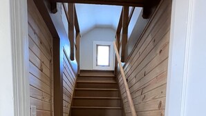 A wooden staircase with a handrail, leading to a small window at the top.