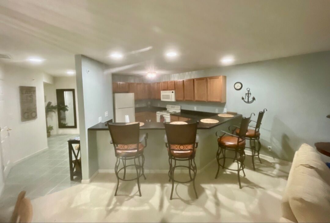A modern kitchen with wooden cabinets, a central island with bar stools, and a refrigerator.