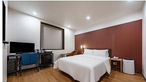 Une chambre d’hôtel moderne dotée d’un grand lit, d’un bureau avec un ordinateur, d’une télévision et d’une fenêtre avec des stores.