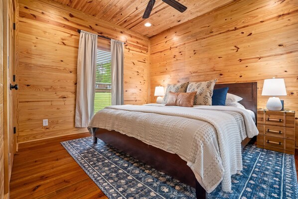 A wooden-paneled bedroom with a bed, nightstands, and a patterned rug.