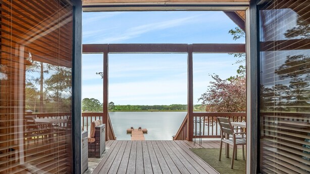 A wooden deck with a bench and a table, overlooking a lake.