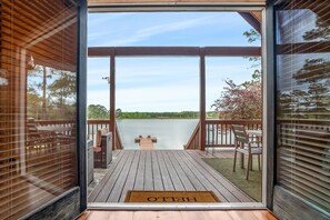A wooden deck with a bench and a table, overlooking a lake.
