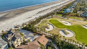 Luchtbeeld van een landgoed aan de kust met een golfbaan, een strand en woongebouwen.