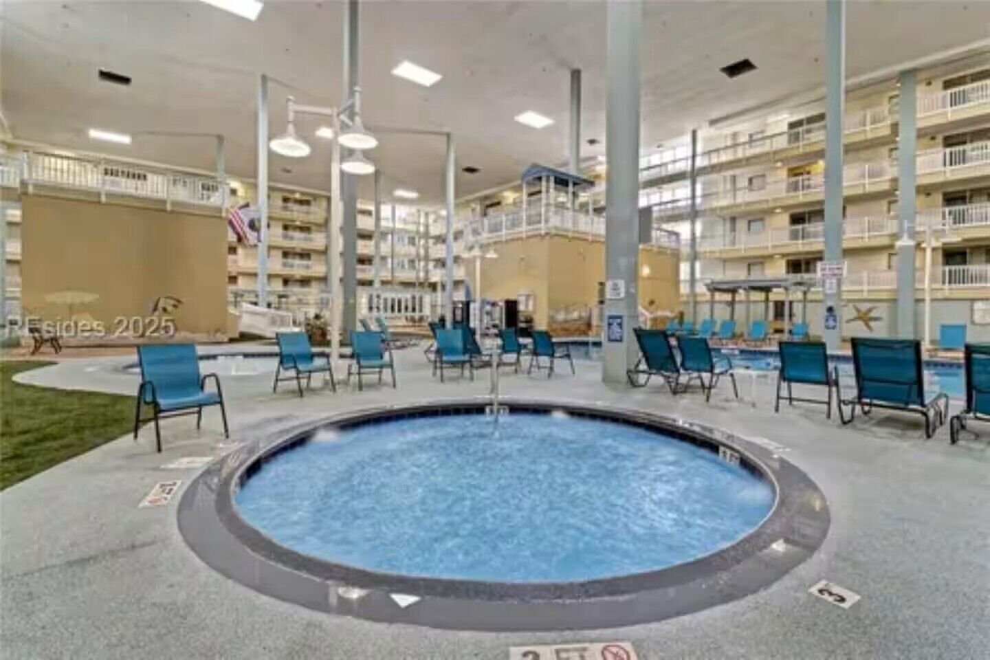A pool area with lounge chairs and a hot tub, surrounded by a multi-story building with balconies.