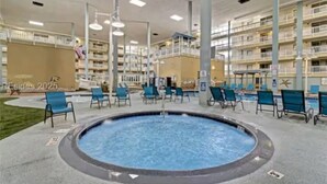 Een zwembad met ligbedden en een jacuzzi, omgeven door een meerlaags gebouw met balkons.