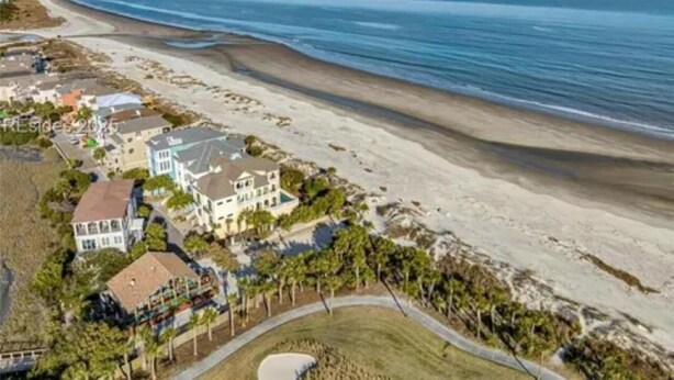 Een kustgebied met woonhuizen direct aan het strand, waaronder woningen met grote ramen en balkons, en een zandstrand.