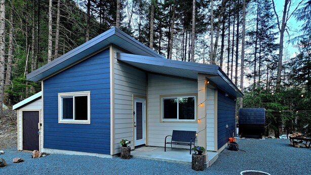 Una casa moderna con fachada azul, dos ventanas, una puerta y un banco en el exterior.