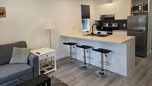 Una cocina moderna con una isla central, taburetes de bar, un refrigerador y un comedor con sofá y una mesita.
