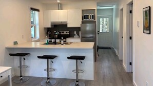 Una cocina moderna con una isla central, taburetes de bar, electrodomésticos de acero inoxidable y vistas al área de estar contigua.