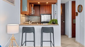 A modern kitchen with wooden cabinets, a stainless steel refrigerator, granite countertop, and two bar stools.