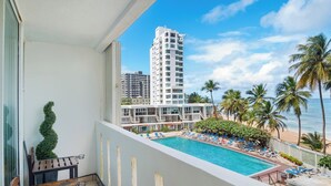 A balcony with a view of a pool, lounge chairs, and palm trees.