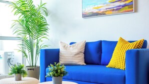A blue sofa with two pillows, a potted plant, and a painting on the wall.