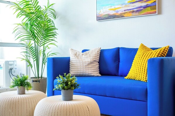 Un sofá azul con dos almohadas, una planta en maceta y un cuadro en la pared.