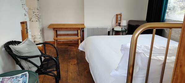 A hotel room with a bed, a wooden nightstand, a chair, a table, and a window with a view.