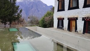 A building with a pool, a mountain backdrop, and a tree in the foreground. - LaMaiSon (Garze)