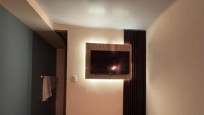 A hallway with a flat-screen TV mounted on the wall, a towel hanging on a rack, and a door leading to another room.