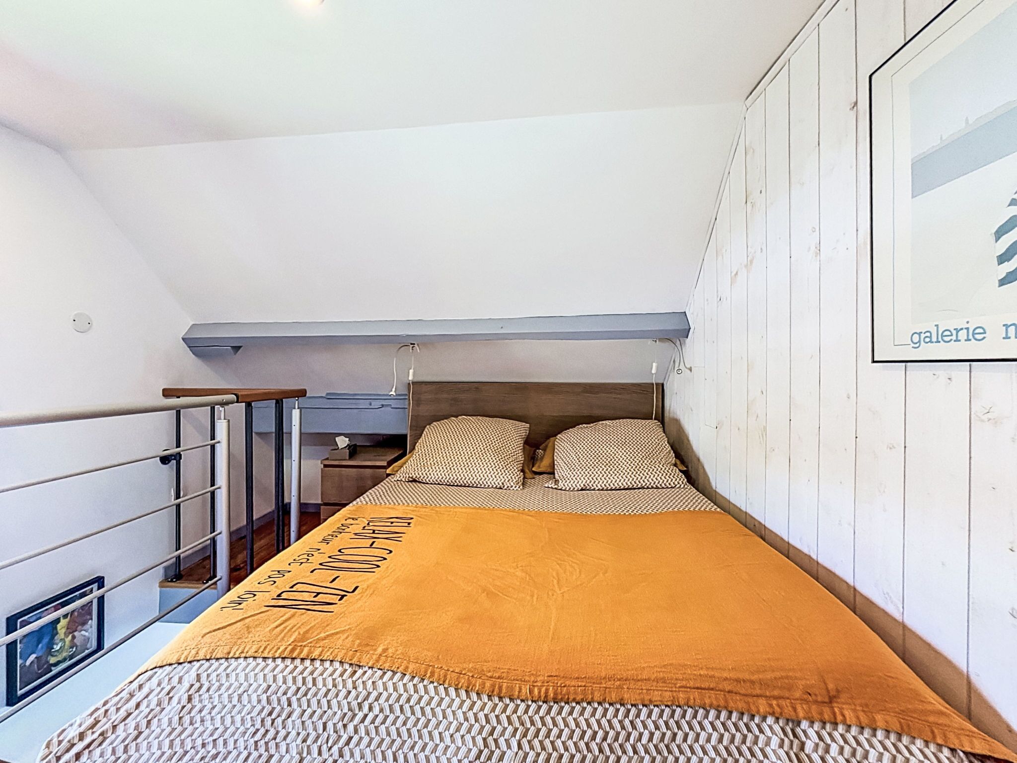 Una habitación pequeña con una cama individual, cabecera de madera, mesita de noche y un cuadro enmarcado en la pared.