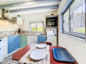 A compact kitchen with blue cabinets, a dining table set for two, a microwave, and a refrigerator.
