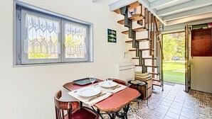 Ein Essbereich mit einem für zwei Personen gedeckten Tisch, einem Fenster mit Spitzenvorhängen, einer Treppe und Blick auf den Garten.