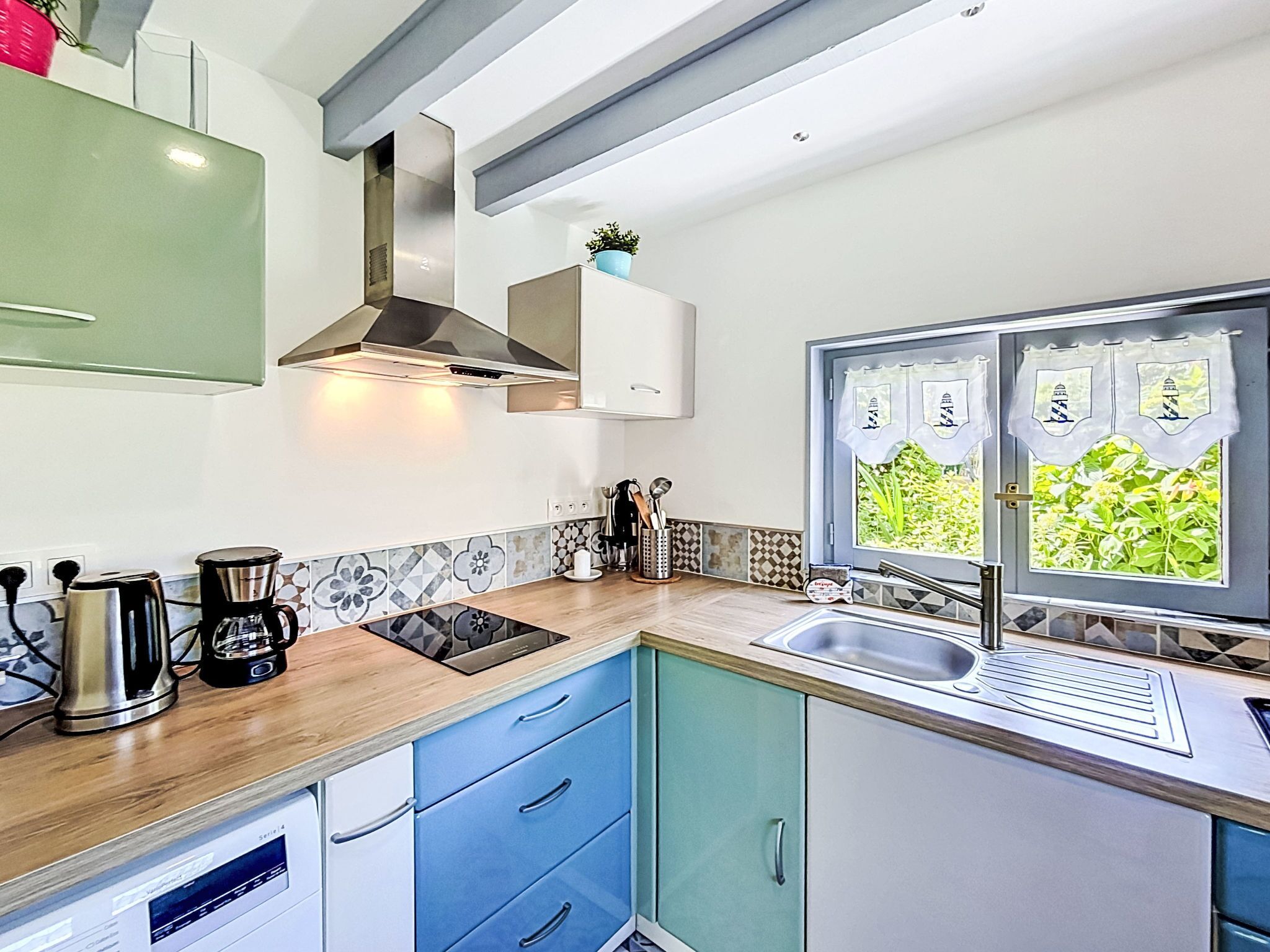 A modern kitchen with a built-in stove, a sink, and a window with decorative curtains.