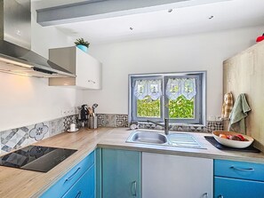 A modern kitchen with blue cabinets, a black induction cooktop, a double sink, and a window with curtains.