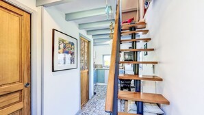 Ein Flur mit einer Holztür, einem gerahmten Bild an der Wand, einem gefliesten Boden und einer Treppe mit Holzstufen und Metallgeländern.