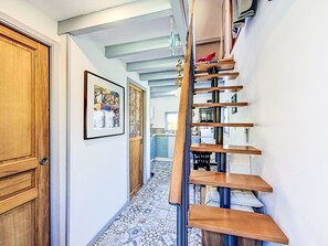 A hallway with a staircase, a wooden door, a framed picture, and a tiled floor.