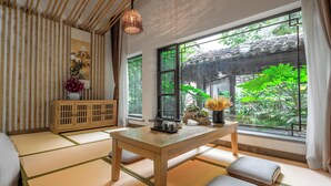 Una habitación tradicional japonesa con suelo de tatami, una mesa de madera y vistas a un jardín a través de amplias ventanas.