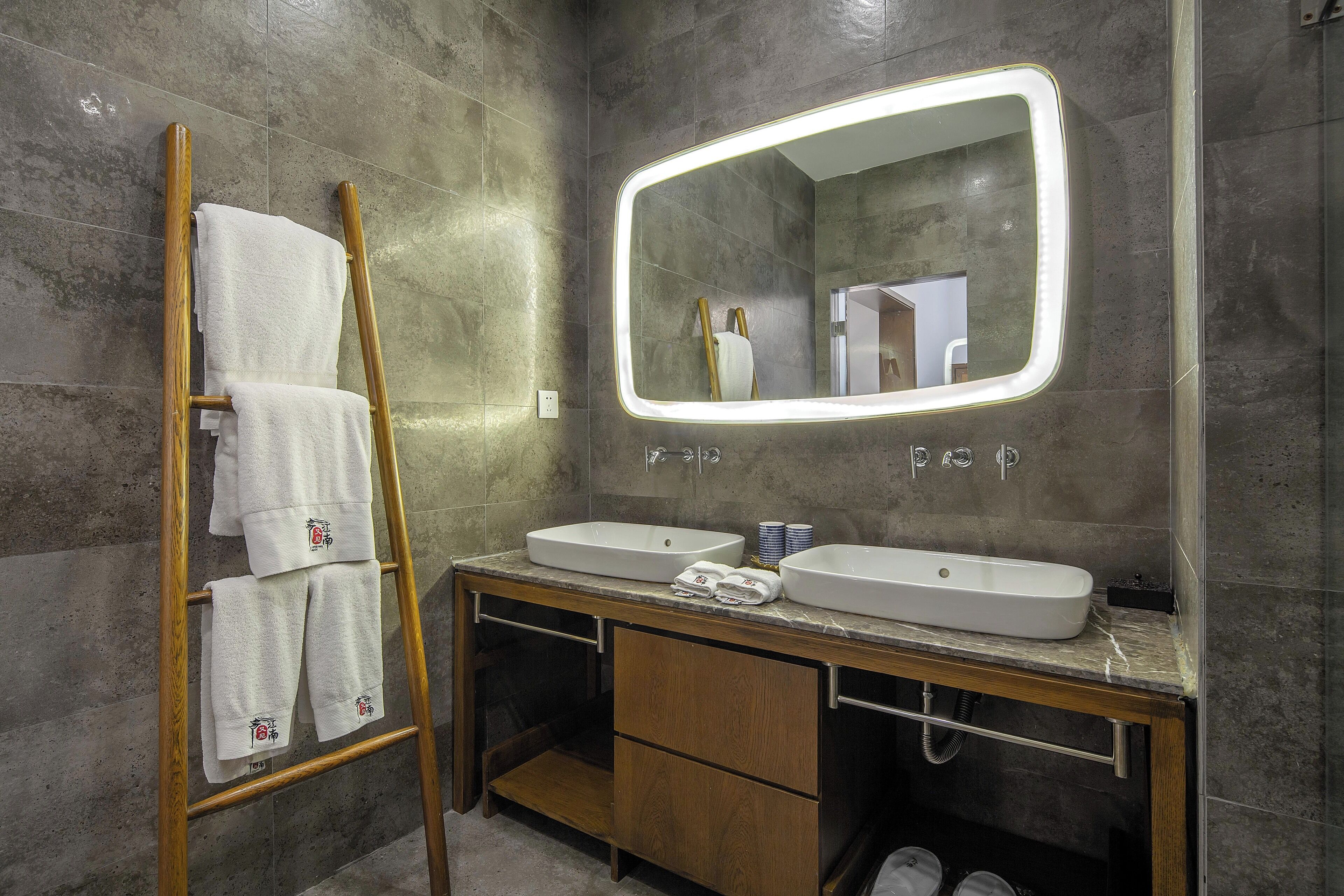 A bathroom with two sinks, a wooden ladder with towels, and a mirror with lights.
