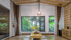 Una habitación con una mesa de madera, bancos acolchados, una lámpara colgante y ventanas amplias con cortinas.