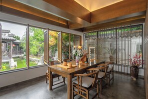 A dining area with a wooden table and chairs, large windows with a view of a traditional building and greenery, and a decorative vase with flowers. - nanjing youjianjiangnan Homestay (Nanjing)