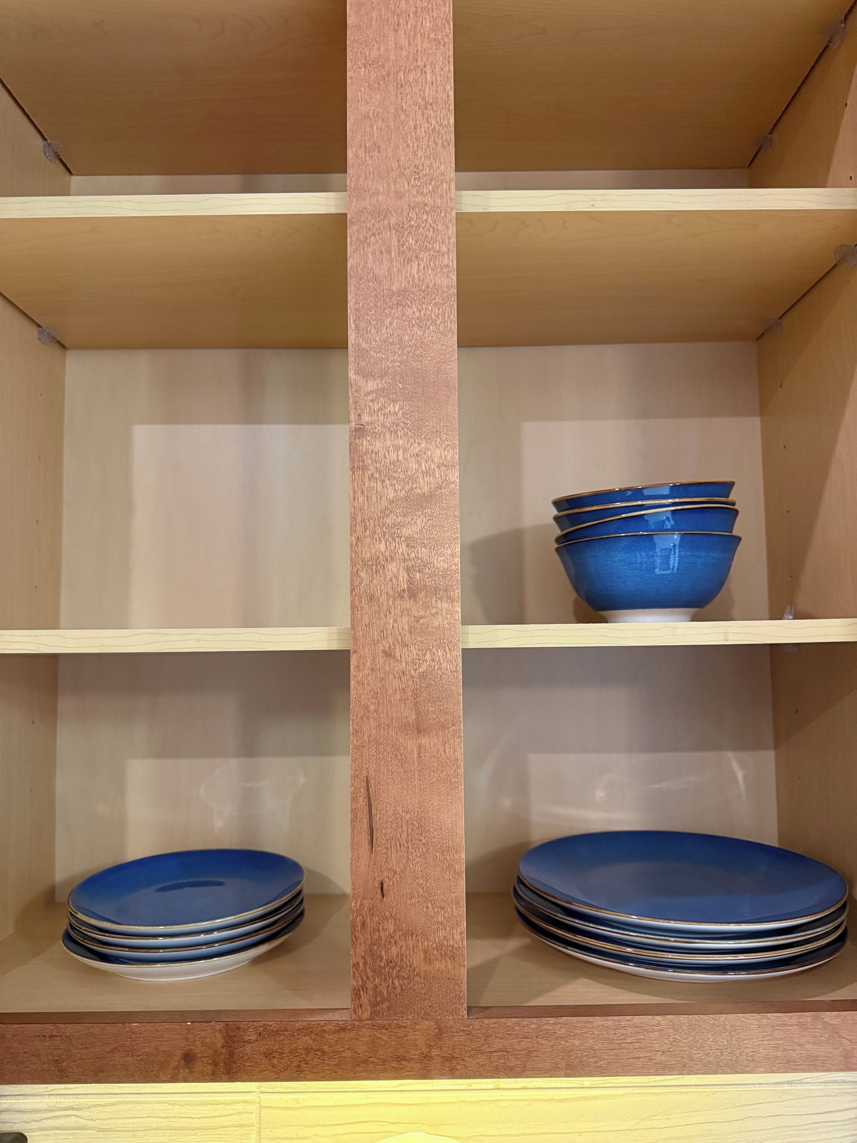 A wooden cabinet with two shelves, each holding stacks of blue plates.