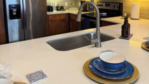 Een moderne keuken met houten kastjes, roestvrijstalen apparatuur en een centraal eiland met een spoelbak en een magnetron erboven.