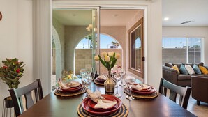 Un coin repas avec une table dressée pour quatre personnes, comprenant des assiettes, des verres et un vase avec des fleurs.