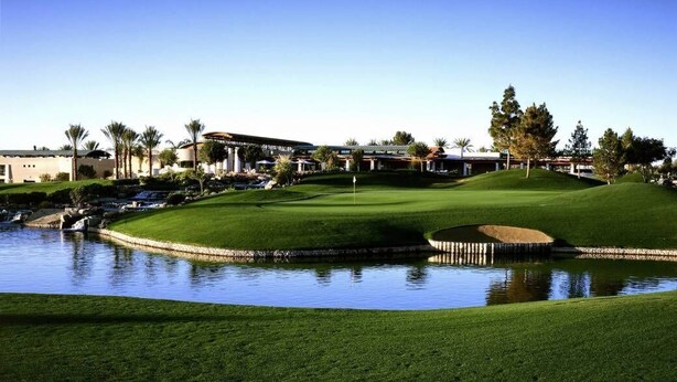 Un parcours de golf avec un étang, une pelouse bien entretenue et un club-house en arrière-plan.