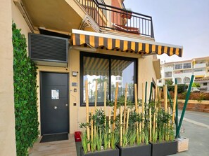 A building with a black door, a window with a striped awning, and a balcony with a railing.