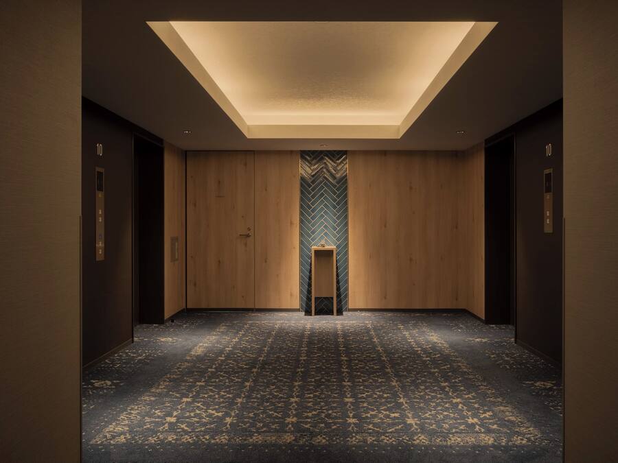 Un pasillo con alfombra estampada, paredes de madera y una columna central con diseño en espiga.