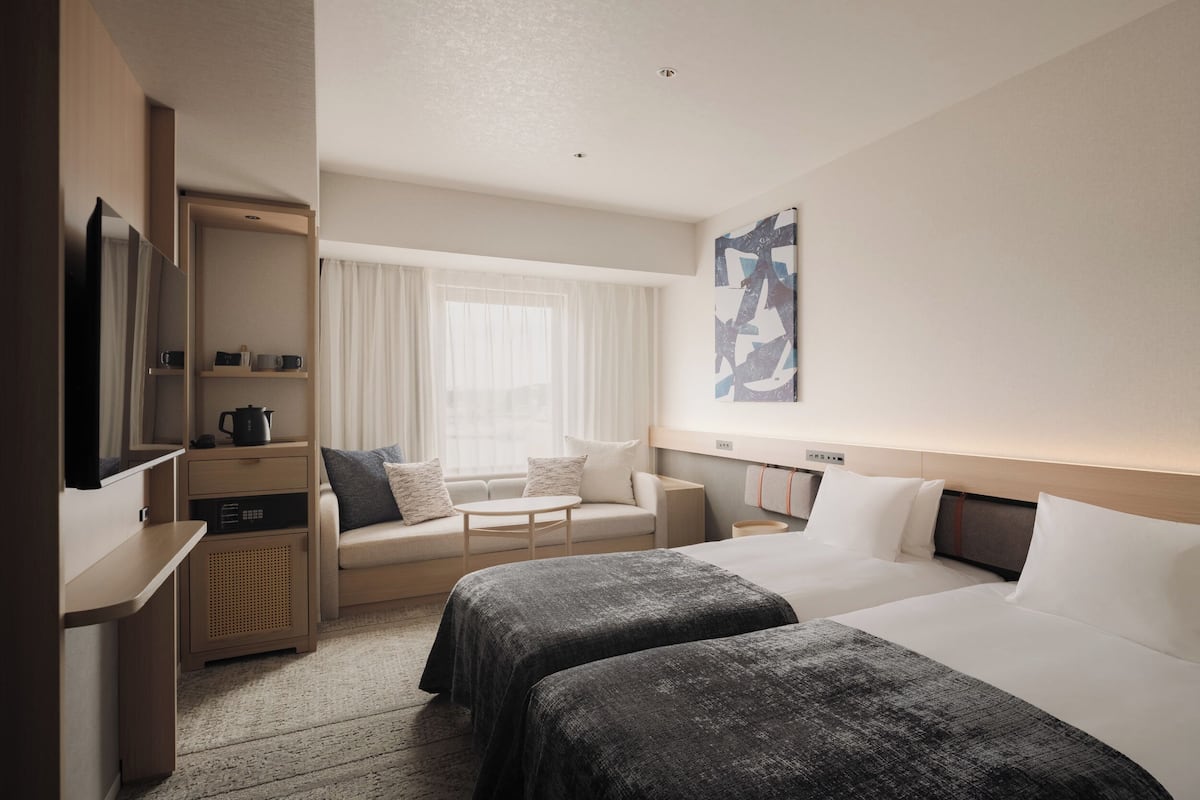 A hotel room with two beds, a sofa, a TV, a desk, and a window with curtains.