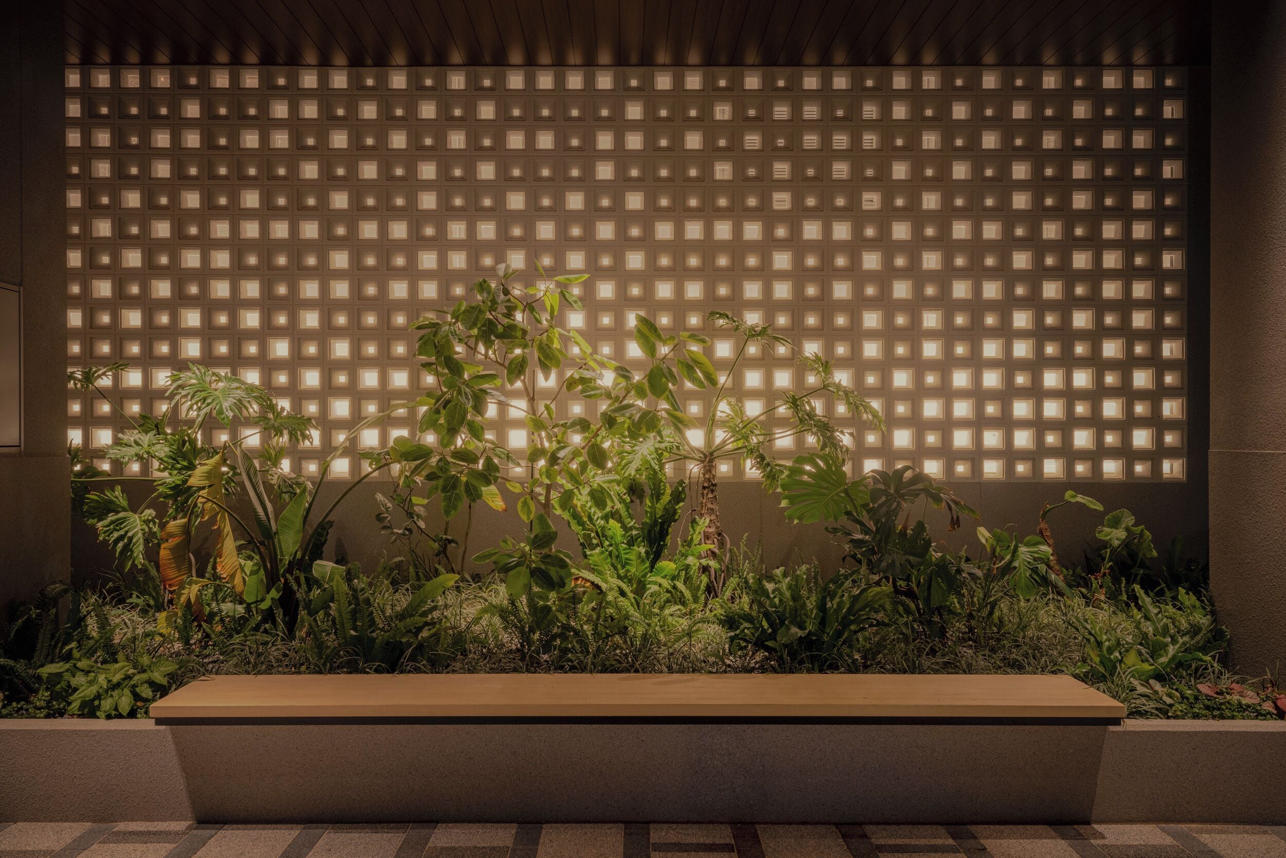 A modern outdoor area with a geometric light panel and a planter with various plants.